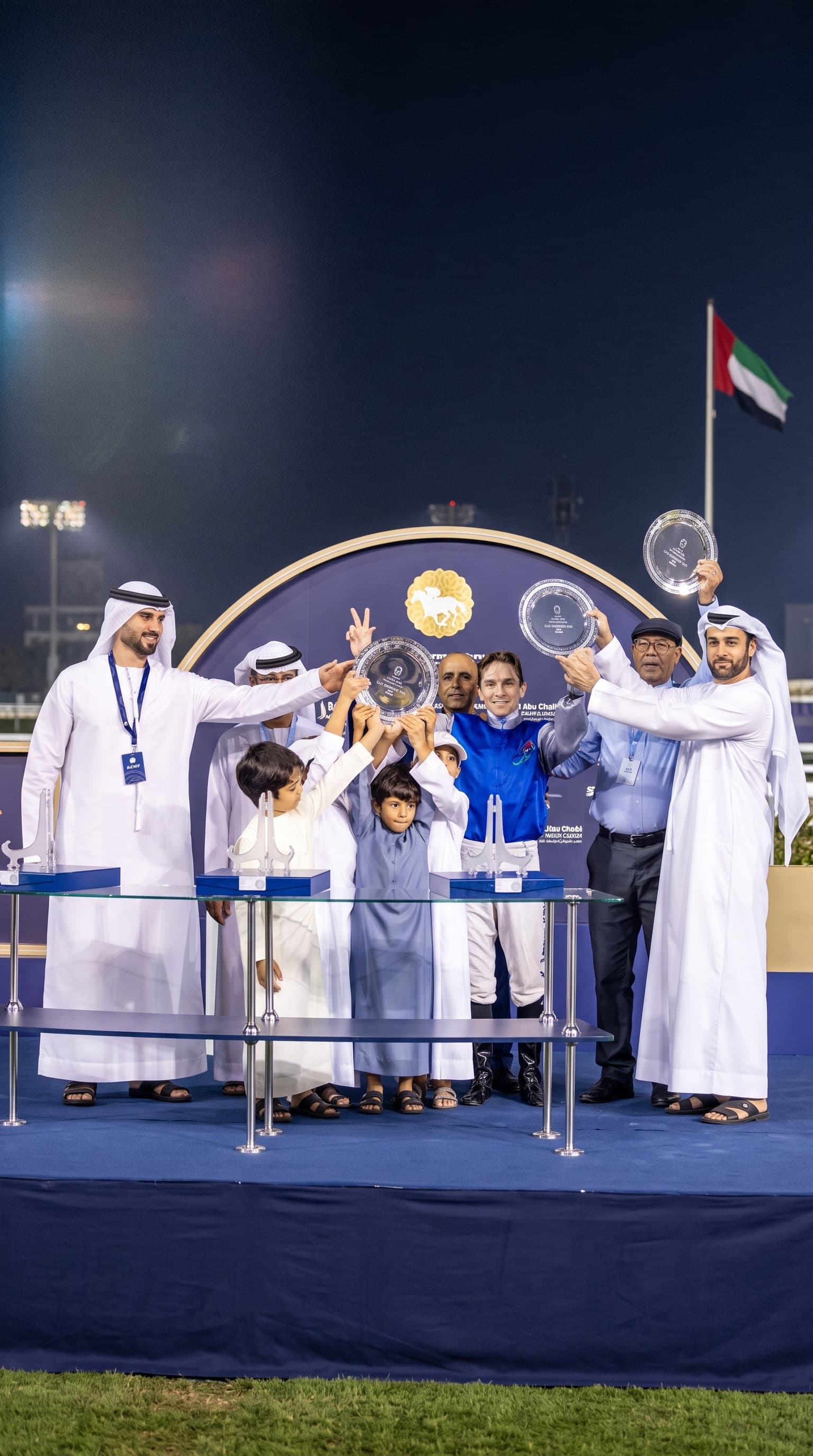 The jockey in blue silks and the winning team hold up trophy plates at the presentation at Abu Dhabi