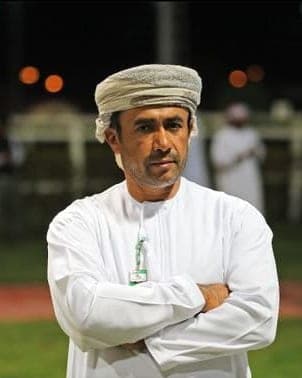 Ibrahim Al Hadhrami in a white dishdasha and patterned turban, arms folded on the racecourse at night