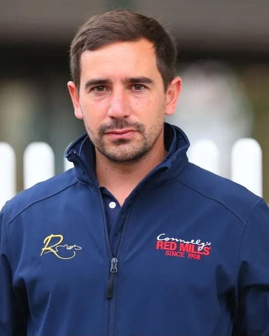 Jérôme Reynier in a navy branded jacket in front of a white picket fence
