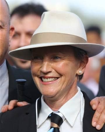 Mme J.F. Bernard in a cream fedora and striped tie, smiling in the winner's enclosure